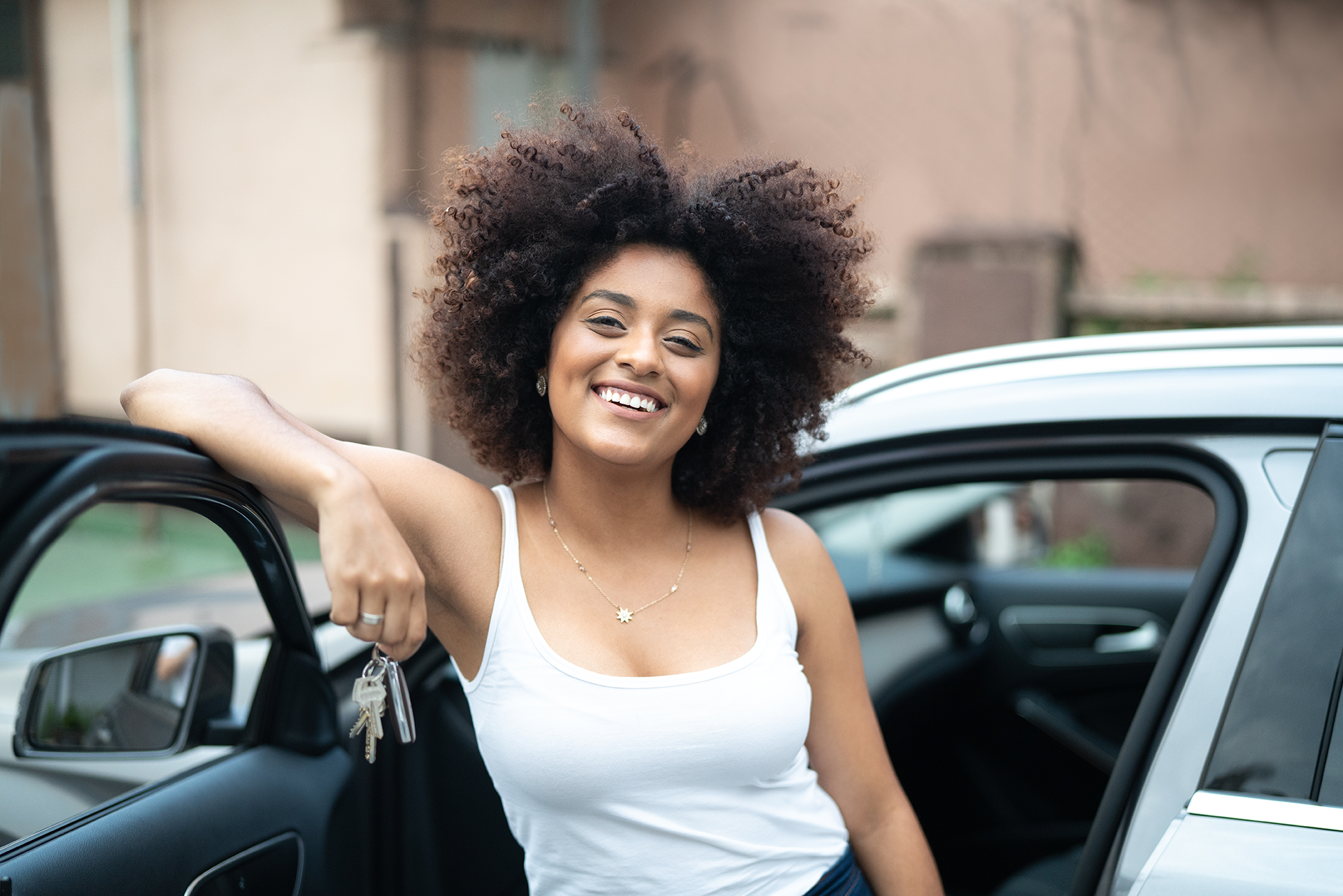 A young person smiling next to their new car