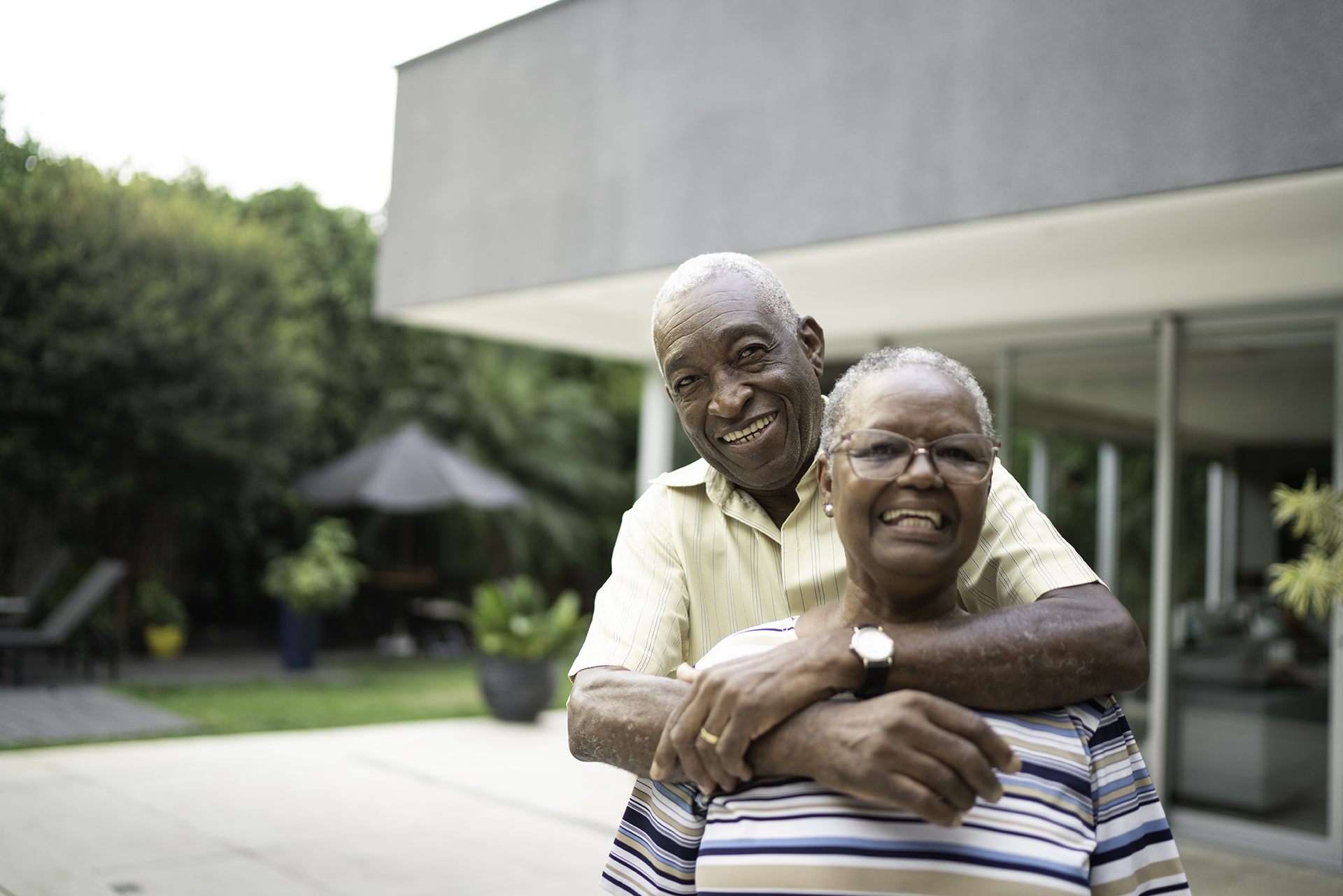 A smiling elderly couple in front of their home
